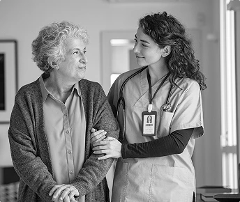 Starsza pacjentka i jej opiekunka wspołnie idą przez korytarz